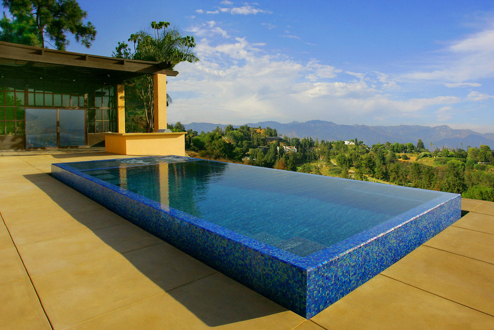 This is an example of a mid-sized contemporary backyard rectangular infinity pool in Los Angeles with a water feature and concrete slab.