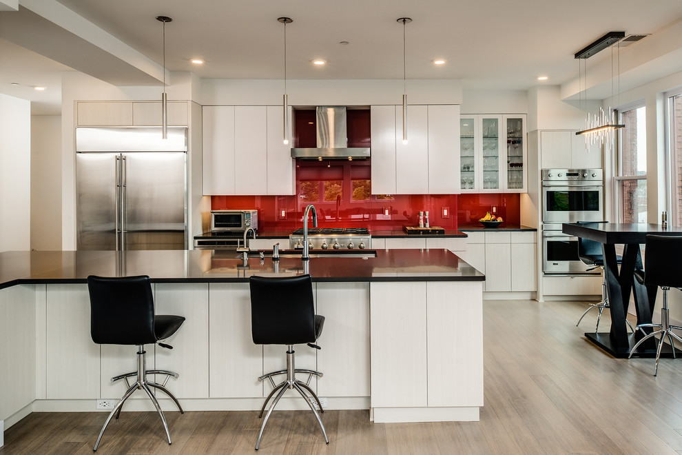 Design ideas for a contemporary eat-in kitchen in Other with an undermount sink, flat-panel cabinets, quartz benchtops, red splashback, glass sheet splashback, stainless steel appliances, light hardwood floors, with island and light wood cabinets.