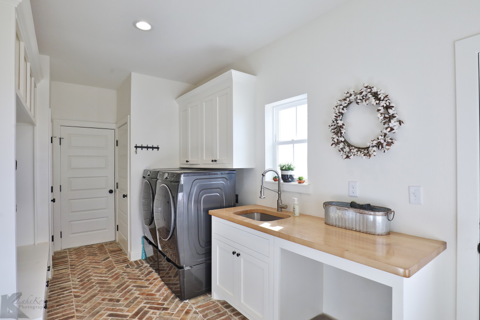 Large country utility room in Other with an undermount sink, shaker cabinets, white cabinets, wood benchtops, white walls, brick floors, a side-by-side washer and dryer, red floor, brown benchtop and decorative wall panelling.