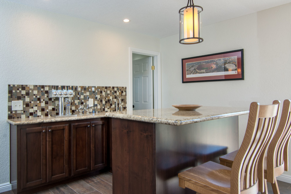 Home bar - huge traditional l-shaped ceramic tile home bar idea in Los Angeles with recessed-panel cabinets, granite countertops, white cabinets, beige backsplash and stone tile backsplash