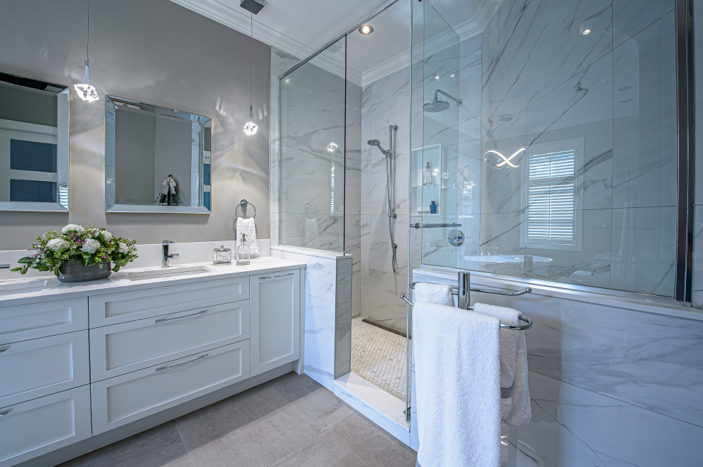 Mid-sized transitional master bathroom in Montreal with shaker cabinets, white cabinets, a freestanding tub, a corner shower, a one-piece toilet, white tile, ceramic tile, grey walls, ceramic floors, an undermount sink, engineered quartz benchtops, grey floor, a hinged shower door, white benchtops, a double vanity and a freestanding vanity.
