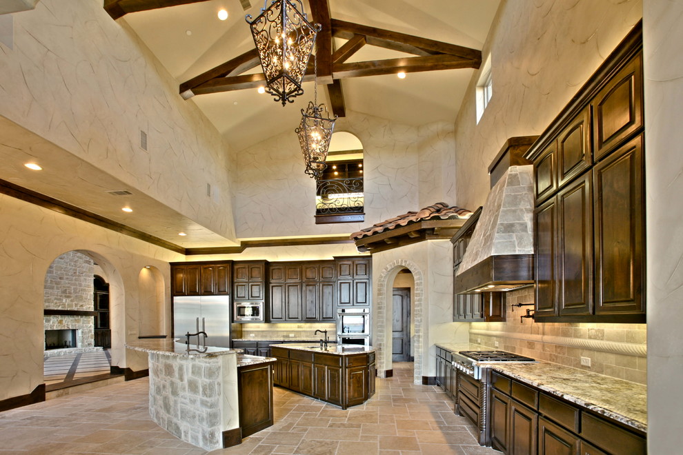 Inspiration for an expansive mediterranean u-shaped eat-in kitchen in Dallas with recessed-panel cabinets, dark wood cabinets, beige splashback, cement tile splashback, travertine floors, multiple islands, an undermount sink, granite benchtops and stainless steel appliances.