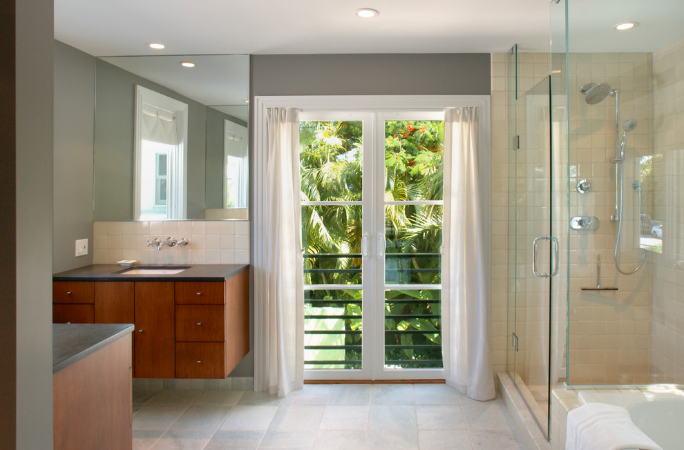 This is an example of a large contemporary master bathroom in Miami with an undermount sink, flat-panel cabinets, medium wood cabinets, a drop-in tub, a corner shower, beige tile, porcelain tile, grey walls, ceramic floors, concrete benchtops, grey floor, a hinged shower door and grey benchtops.