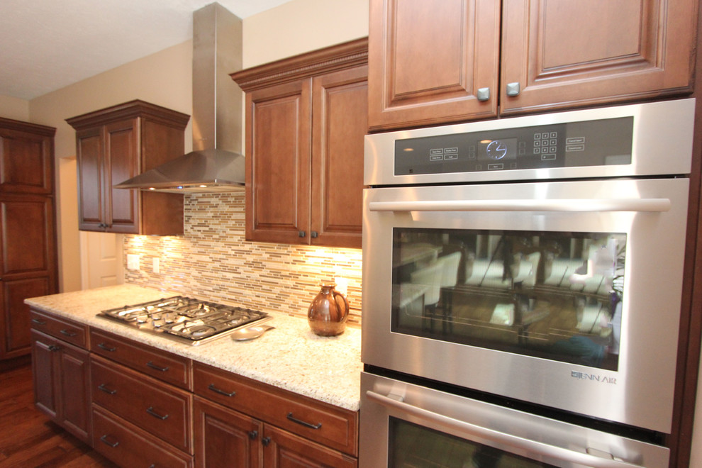 Example of a large transitional l-shaped medium tone wood floor eat-in kitchen design with a farmhouse sink, raised-panel cabinets, medium tone wood cabinets, granite countertops, beige backsplash, glass tile backsplash, stainless steel appliances, beige walls and an island