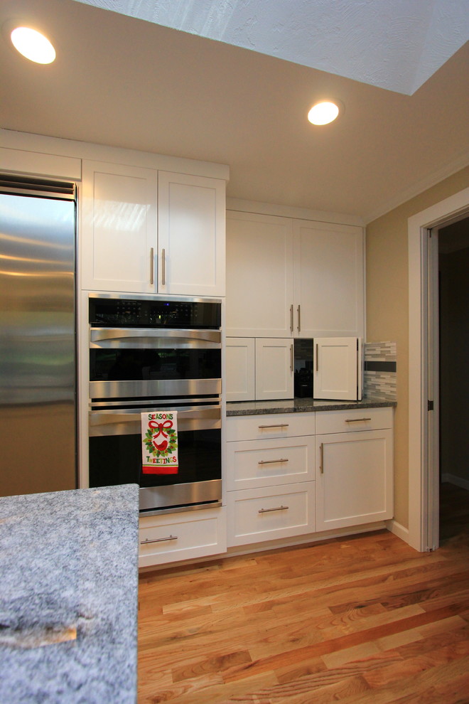 Inspiration for a large transitional u-shaped light wood floor open concept kitchen remodel with an undermount sink, shaker cabinets, white cabinets, granite countertops, multicolored backsplash, mosaic tile backsplash, stainless steel appliances and an island