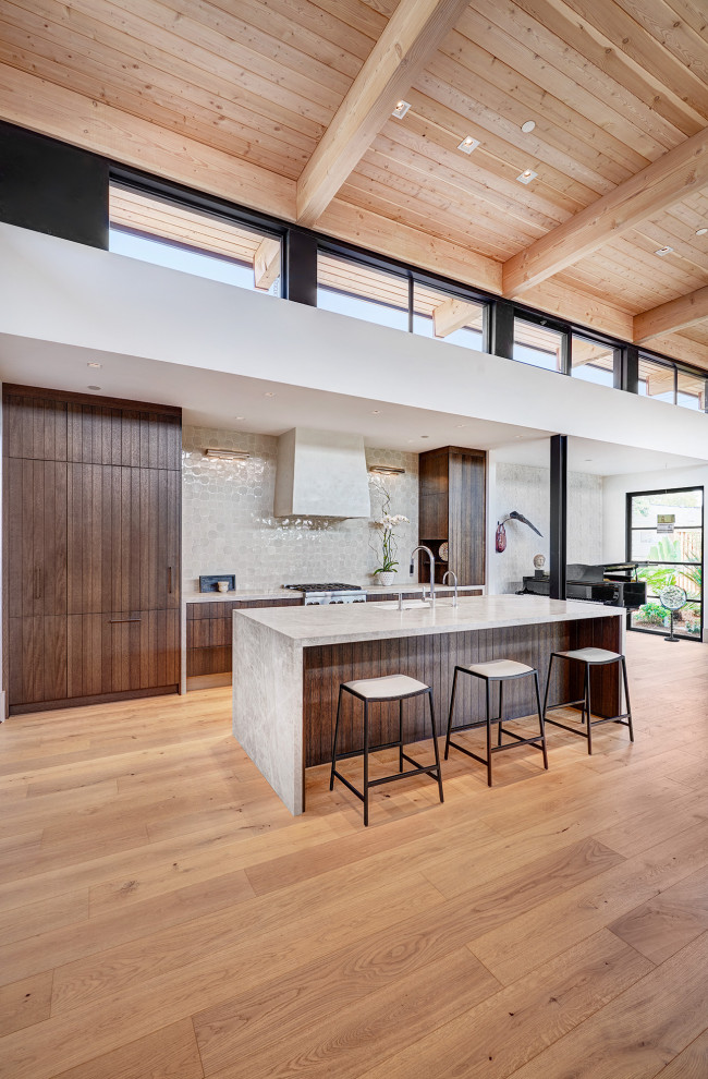This is an example of a mid-sized contemporary galley open plan kitchen in Sacramento with an undermount sink, flat-panel cabinets, brown cabinets, granite benchtops, beige splashback, ceramic splashback, light hardwood floors, with island, brown floor, grey benchtop, wood and panelled appliances.