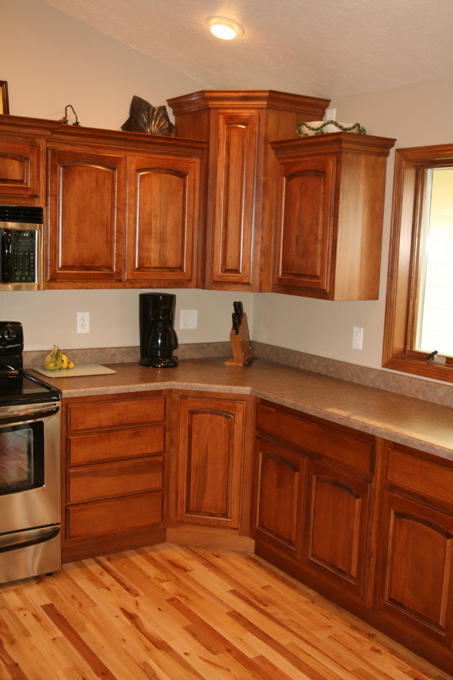 Inspiration for a mid-sized l-shaped light wood floor open concept kitchen remodel with a drop-in sink, raised-panel cabinets, medium tone wood cabinets, laminate countertops, stainless steel appliances and an island
