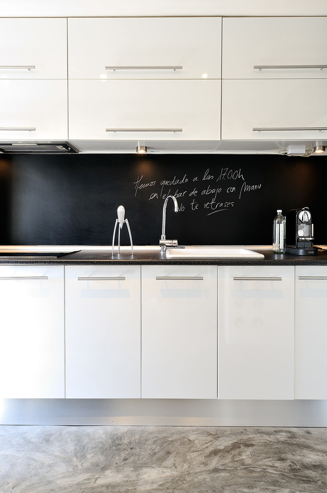 Small contemporary single-wall eat-in kitchen in Madrid with a drop-in sink, flat-panel cabinets, white cabinets, black splashback, panelled appliances, concrete floors and no island.