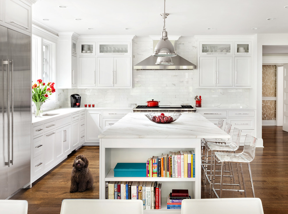 This is an example of a transitional l-shaped open plan kitchen in New York with shaker cabinets, white cabinets, marble benchtops, white splashback, with island and stainless steel appliances.