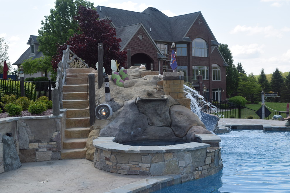 Expansive transitional backyard custom-shaped pool in Detroit with a water slide and stamped concrete.