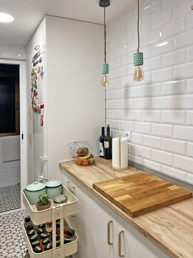 Small scandinavian separate kitchen in Madrid with an undermount sink, flat-panel cabinets, white cabinets, wood benchtops, white splashback, ceramic splashback, stainless steel appliances, ceramic floors, no island, multi-coloured floor and brown benchtop.