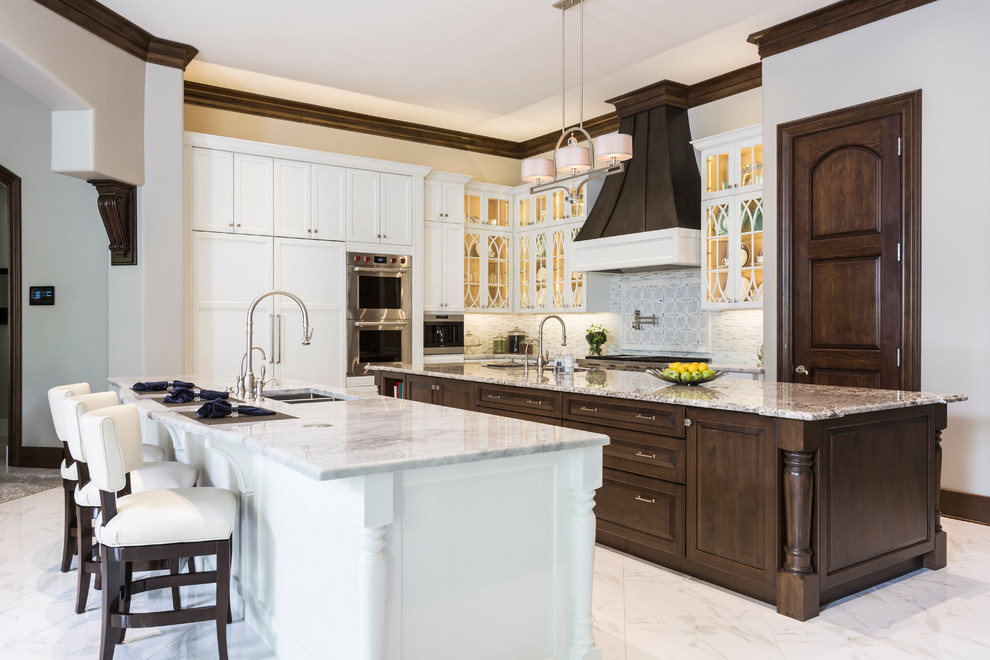 Photo of a transitional l-shaped separate kitchen in Houston with a double-bowl sink, glass-front cabinets, white cabinets, marble benchtops, white splashback, ceramic splashback, stainless steel appliances, porcelain floors and multiple islands.
