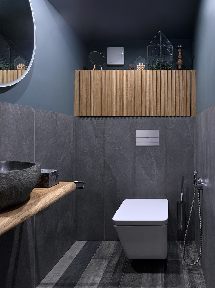 Contemporary powder room in Moscow with a wall-mount toilet, porcelain tile, porcelain floors, a vessel sink, gray tile, grey walls, wood benchtops and multi-coloured floor.