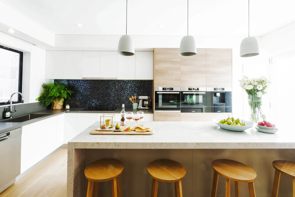 This is an example of a large contemporary l-shaped kitchen in Melbourne with an undermount sink, flat-panel cabinets, light wood cabinets, stainless steel appliances, light hardwood floors and with island.