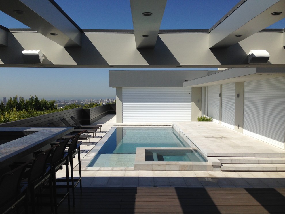 This is an example of a mid-sized modern rooftop rectangular infinity pool in Los Angeles with a hot tub and natural stone pavers.