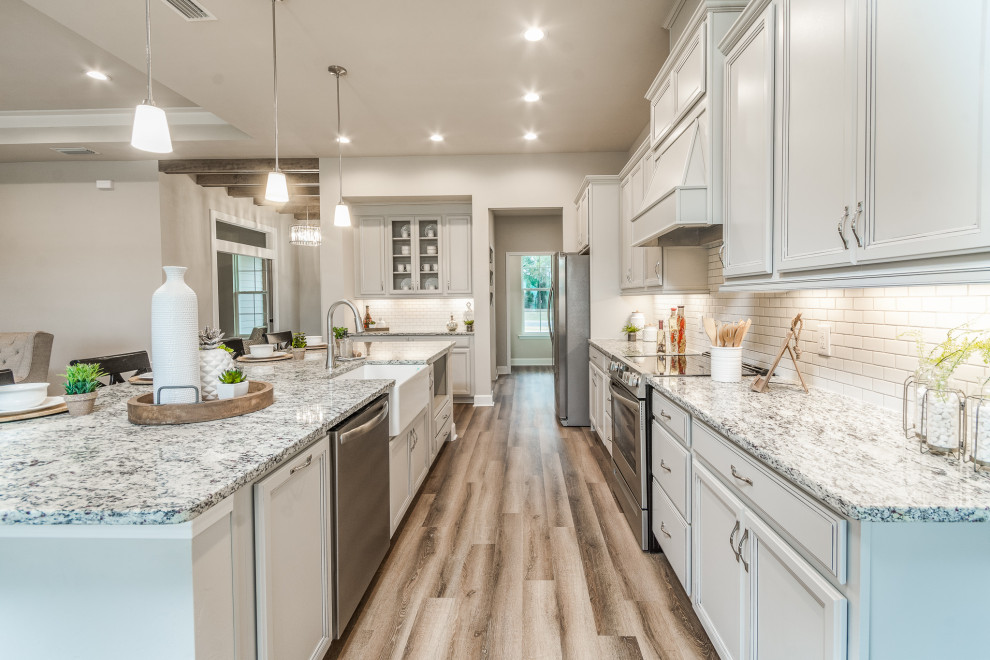 Example of a mid-sized transitional galley vinyl floor and multicolored floor eat-in kitchen design with a farmhouse sink, recessed-panel cabinets, granite countertops, white backsplash, subway tile backsplash, stainless steel appliances, an island, multicolored countertops and gray cabinets