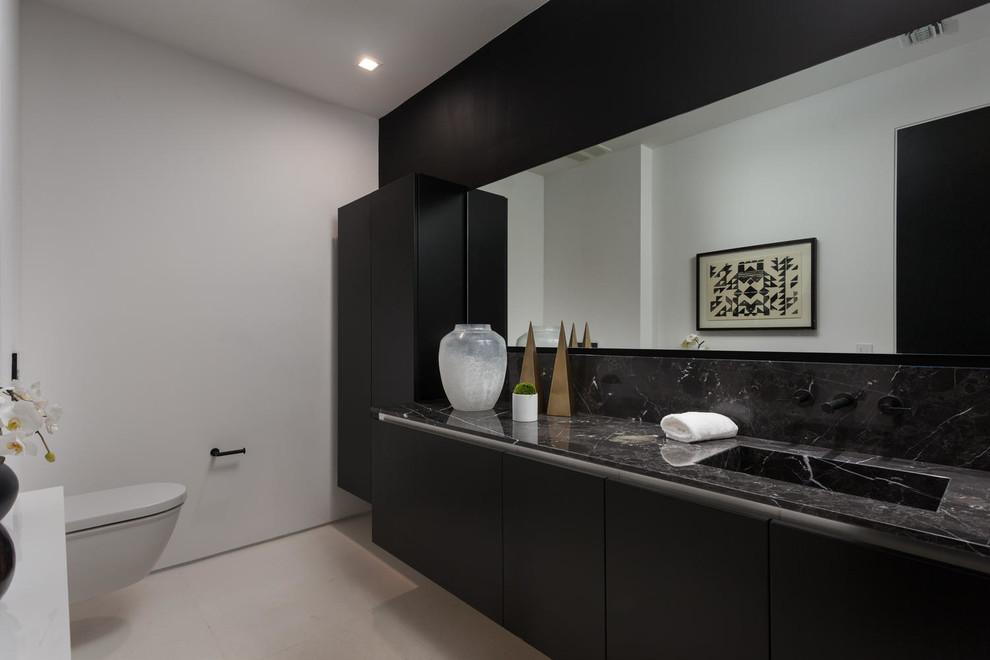 Large modern powder room in Los Angeles with flat-panel cabinets, black cabinets, a wall-mount toilet, black tile, beige tile, stone slab, white walls, porcelain floors, an integrated sink and marble benchtops.