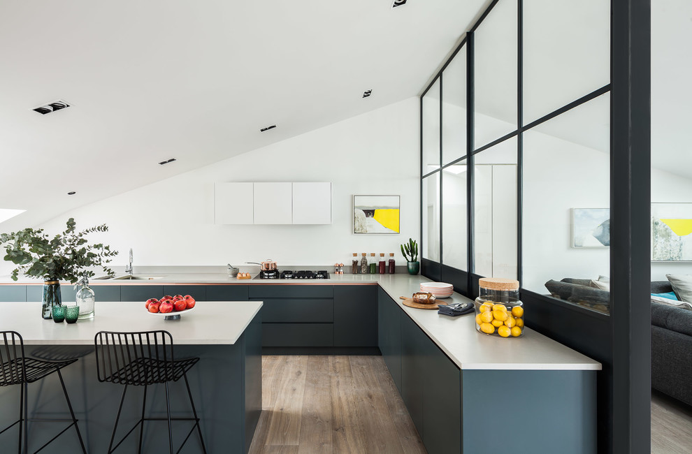 This is an example of a mid-sized contemporary l-shaped open plan kitchen in London with a double-bowl sink, flat-panel cabinets, blue cabinets, concrete benchtops, with island and brown floor.