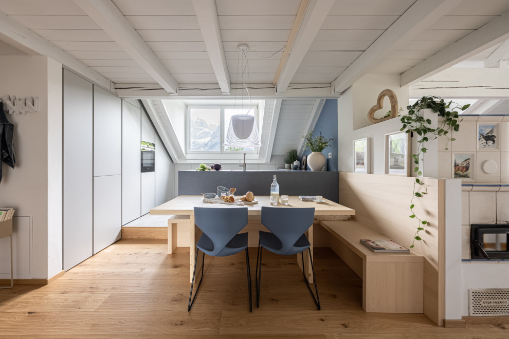 Cette image montre une salle à manger nordique avec un mur blanc, parquet foncé, un poêle à bois, un sol marron et poutres apparentes.