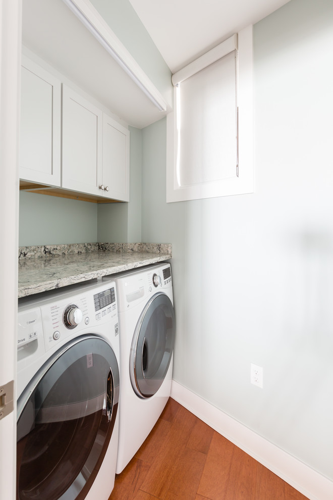 This is an example of a beach style single-wall laundry cupboard in Other with shaker cabinets, white cabinets, granite benchtops, blue walls, medium hardwood floors, a side-by-side washer and dryer and brown floor.