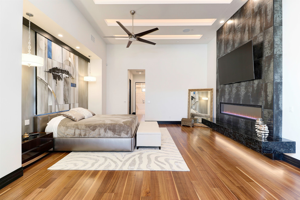 Inspiration for a contemporary bedroom in Phoenix with white walls, medium hardwood floors, a ribbon fireplace, a tile fireplace surround and brown floor.