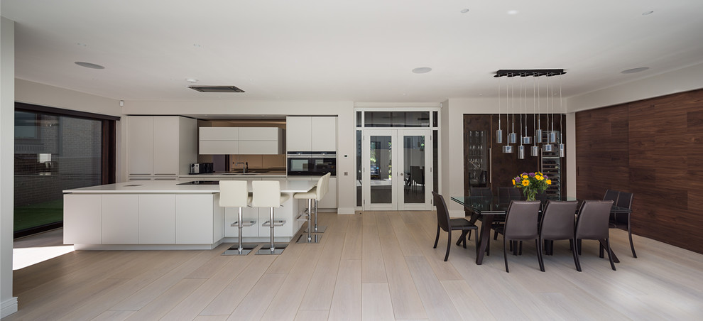 Large single-wall eat-in kitchen in London with an integrated sink, flat-panel cabinets, white cabinets, limestone benchtops, metallic splashback, light hardwood floors, with island, brown floor and white benchtop.
