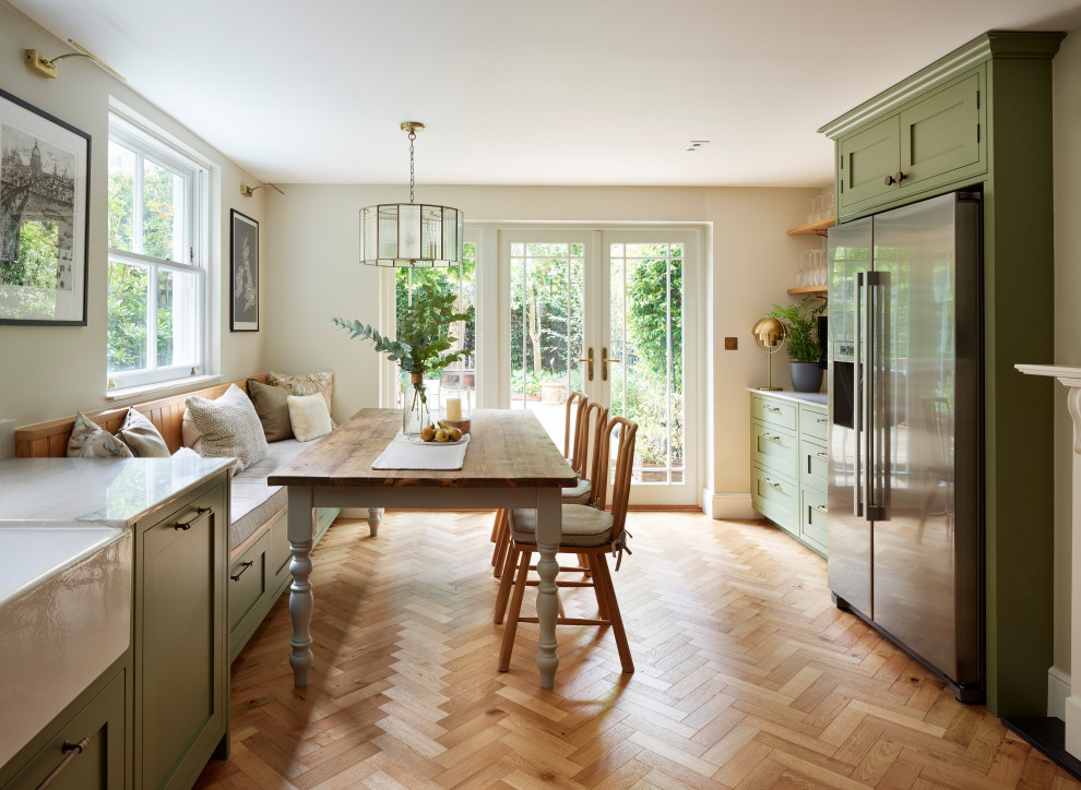 Design ideas for a large traditional u-shaped eat-in kitchen in Gloucestershire with a farmhouse sink, shaker cabinets, green cabinets, quartzite benchtops, white splashback, ceramic splashback, stainless steel appliances, medium hardwood floors, no island, brown floor and multi-coloured benchtop.