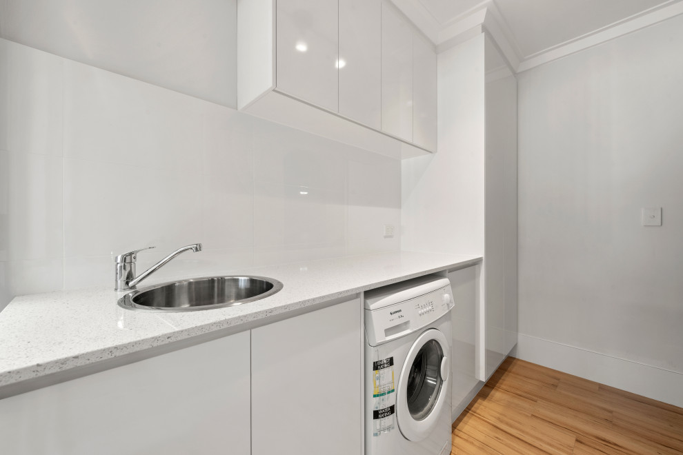 This is an example of a mid-sized modern single-wall dedicated laundry room in Perth with a drop-in sink, shaker cabinets, white cabinets, white walls, yellow floor and white benchtop.