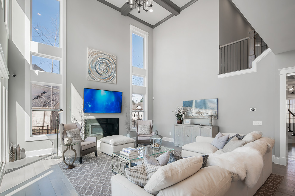 Photo of an expansive transitional open concept living room in Charlotte with grey walls, light hardwood floors, a standard fireplace, a plaster fireplace surround, a built-in media wall and coffered.