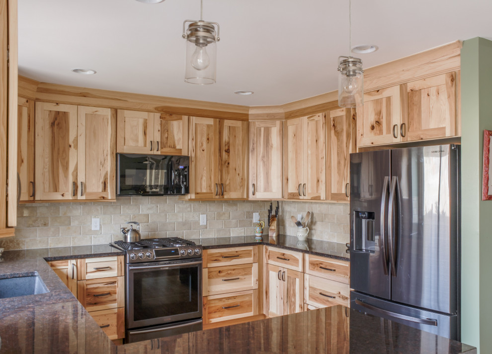 Mid-sized country u-shaped eat-in kitchen in Detroit with an undermount sink, recessed-panel cabinets, light wood cabinets, quartz benchtops, beige splashback, travertine splashback, stainless steel appliances, light hardwood floors, a peninsula, brown floor and black benchtop.