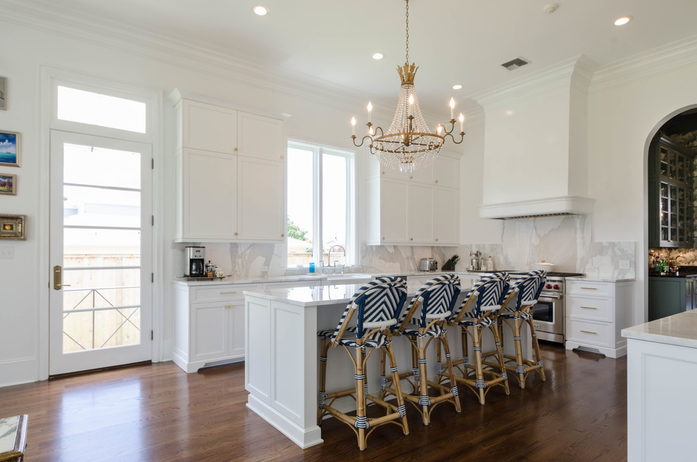 Mid-sized beach style u-shaped kitchen in New Orleans with a farmhouse sink, raised-panel cabinets, white cabinets, marble benchtops, white splashback, stainless steel appliances, dark hardwood floors and with island.