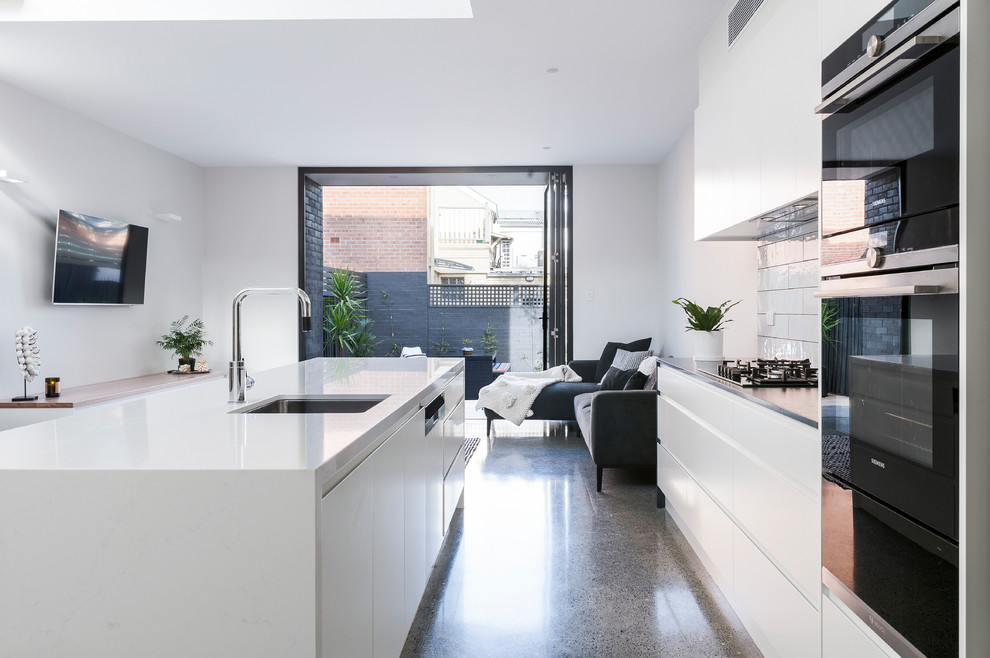 Design ideas for a contemporary galley open plan kitchen in Sydney with an undermount sink, flat-panel cabinets, white cabinets, quartz benchtops, white splashback, subway tile splashback, stainless steel appliances, concrete floors, with island and white benchtop.