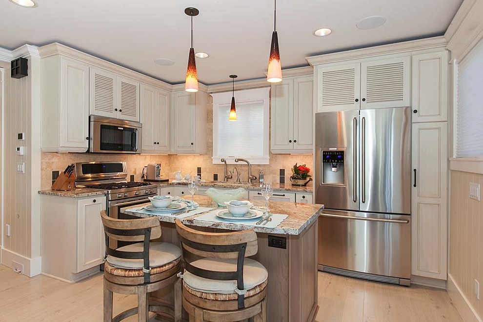 This is an example of a small beach style l-shaped open plan kitchen in Seattle with an undermount sink, louvered cabinets, white cabinets, granite benchtops, beige splashback, stone tile splashback, stainless steel appliances, porcelain floors and with island.