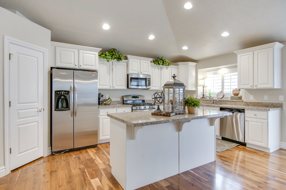 Inspiration for a traditional l-shaped open plan kitchen in Salt Lake City with raised-panel cabinets, white cabinets, beige splashback, stainless steel appliances, light hardwood floors and with island.
