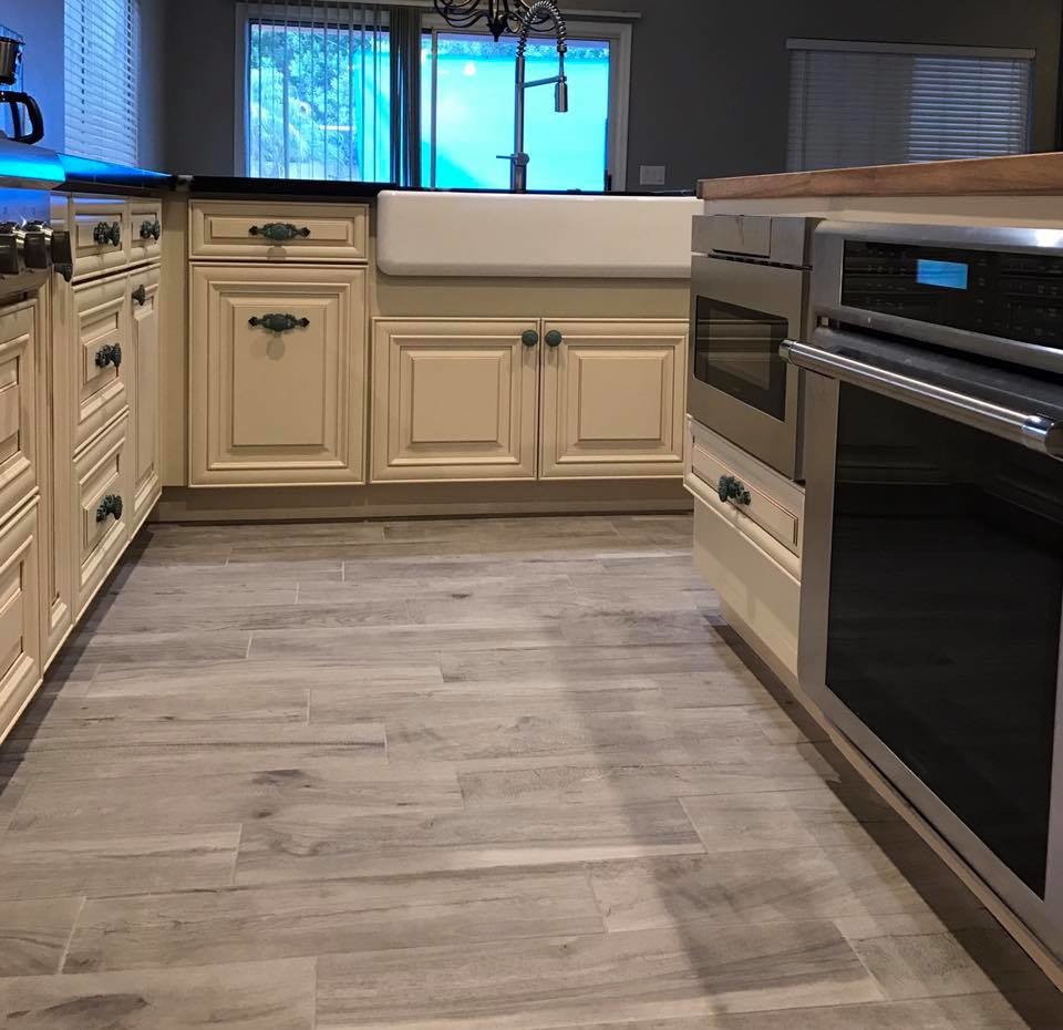 This is an example of a mid-sized transitional l-shaped eat-in kitchen in Phoenix with a farmhouse sink, raised-panel cabinets, beige cabinets, quartz benchtops, multi-coloured splashback, mosaic tile splashback, stainless steel appliances, porcelain floors and with island.