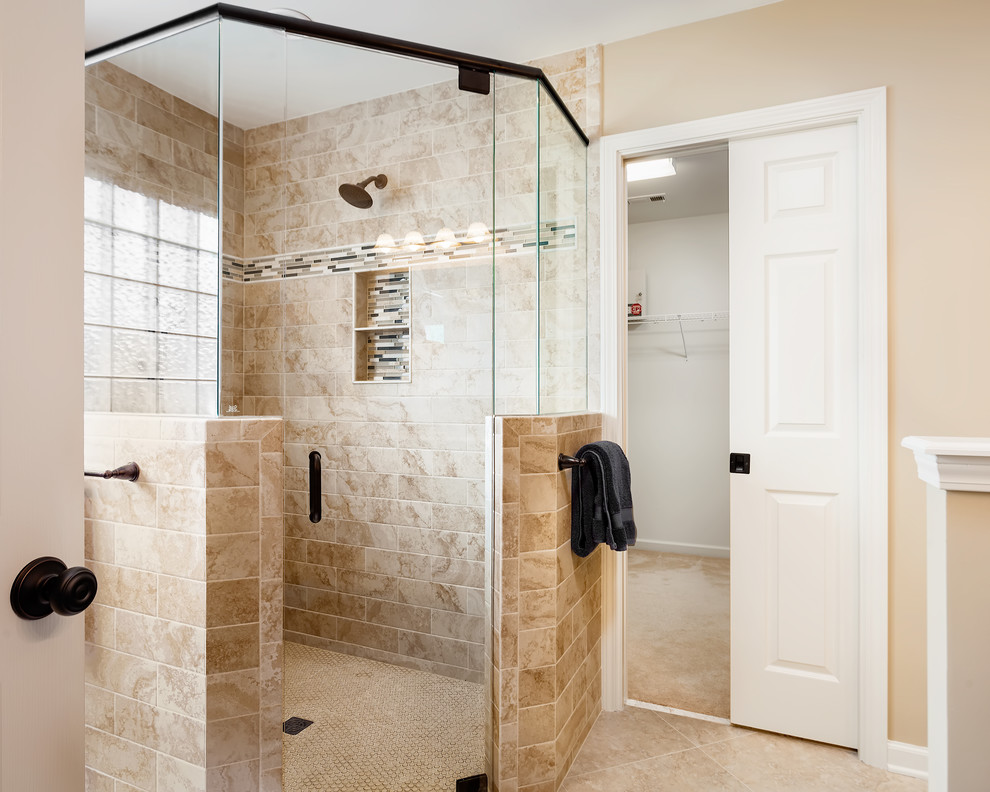 This is an example of a mid-sized traditional master bathroom in Charlotte with furniture-like cabinets, brown cabinets, a curbless shower, a two-piece toilet, beige tile, porcelain tile, beige walls, porcelain floors, an undermount sink, marble benchtops, beige floor and a hinged shower door.