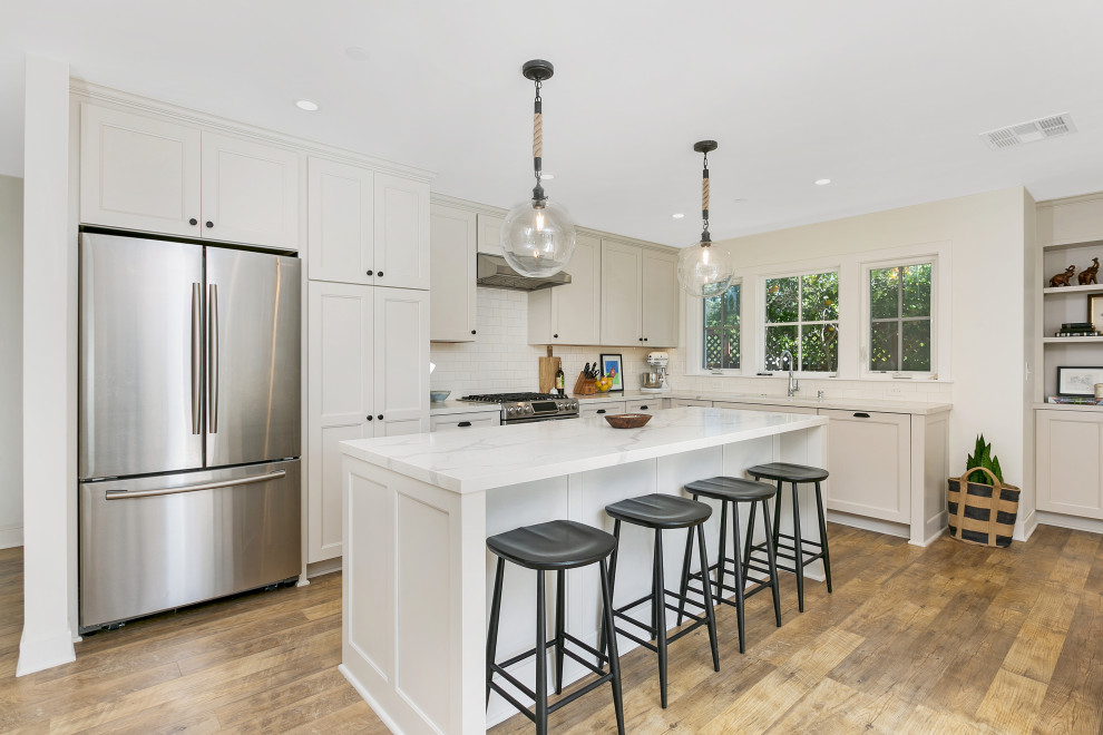 Photo of a mid-sized country l-shaped open plan kitchen in San Diego with an undermount sink, flat-panel cabinets, grey cabinets, quartz benchtops, white splashback, subway tile splashback, stainless steel appliances, vinyl floors, with island, brown floor and white benchtop.