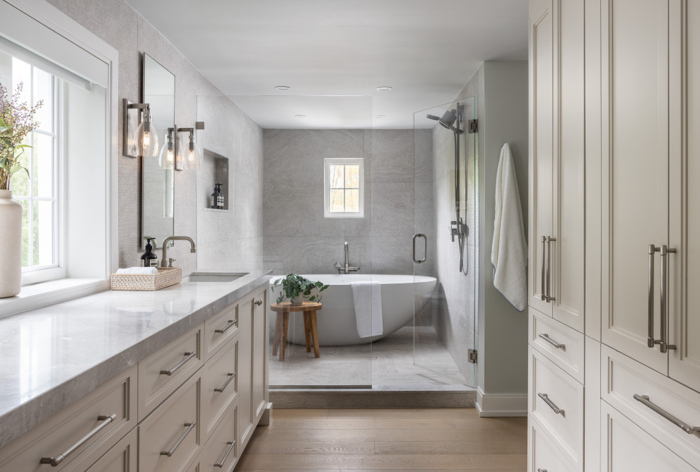 Inspiration for a huge transitional master porcelain tile and gray tile brown floor, double-sink and medium tone wood floor bathroom remodel in Detroit with beige cabinets, an undermount sink, marble countertops, a freestanding vanity, recessed-panel cabinets, gray walls, a hinged shower door and gray countertops