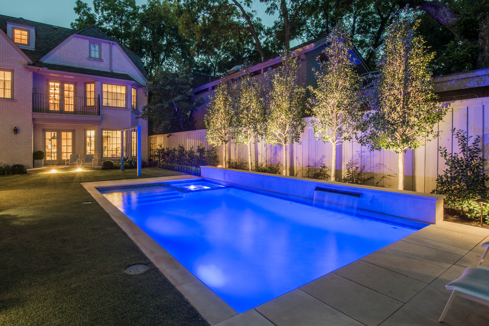 This is an example of a mid-sized transitional backyard rectangular lap pool in Dallas with a water feature and natural stone pavers.
