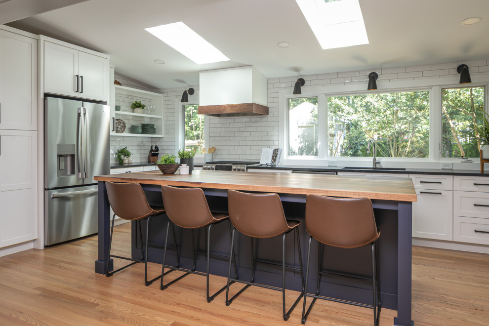 Photo of a large eclectic l-shaped eat-in kitchen in Raleigh with an undermount sink, shaker cabinets, white cabinets, wood benchtops, white splashback, porcelain splashback, stainless steel appliances, medium hardwood floors, with island, brown floor, black benchtop and vaulted.