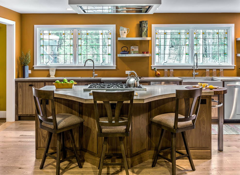 Photo of a mid-sized arts and crafts galley kitchen in Portland Maine with a farmhouse sink, flat-panel cabinets, medium wood cabinets, stainless steel benchtops, orange splashback, stainless steel appliances, light hardwood floors and with island.