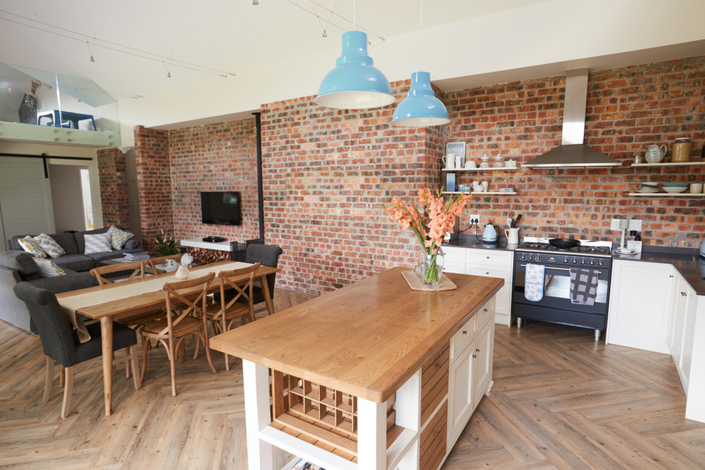 Photo of a large country l-shaped eat-in kitchen in Adelaide with an undermount sink, shaker cabinets, white cabinets, wood benchtops, brick splashback, black appliances, light hardwood floors and with island.