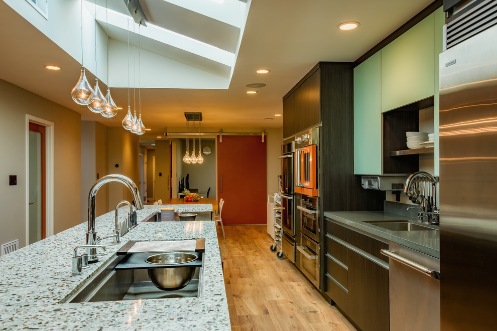 Photo of a large contemporary l-shaped open plan kitchen in San Francisco with an undermount sink, flat-panel cabinets, grey cabinets, recycled glass benchtops, coloured appliances, with island and light hardwood floors.