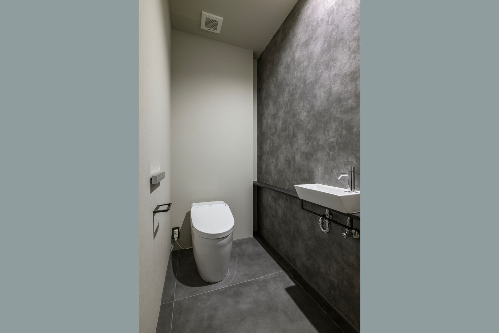 Foto på ett mellanstort funkis svart toalett, med öppna hyllor, svarta skåp, en toalettstol med hel cisternkåpa, grå kakel, cementkakel, grå väggar, klinkergolv i keramik, ett fristående handfat, träbänkskiva och grått golv