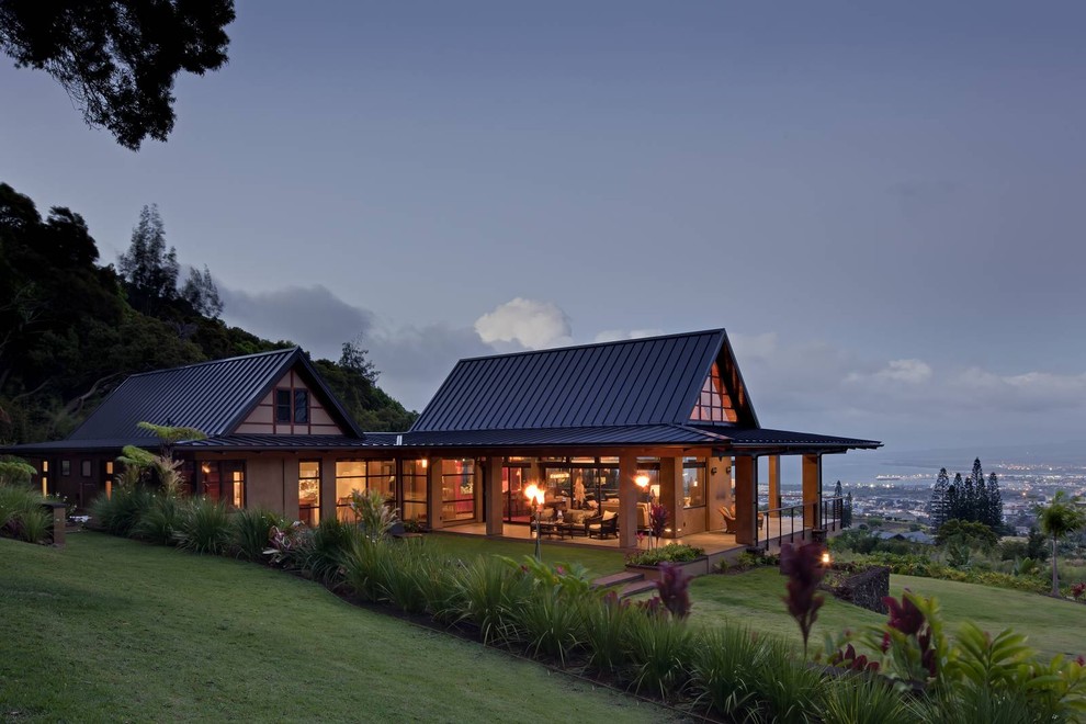 Large tropical two-storey glass beige house exterior in Hawaii with a hip roof and a metal roof.