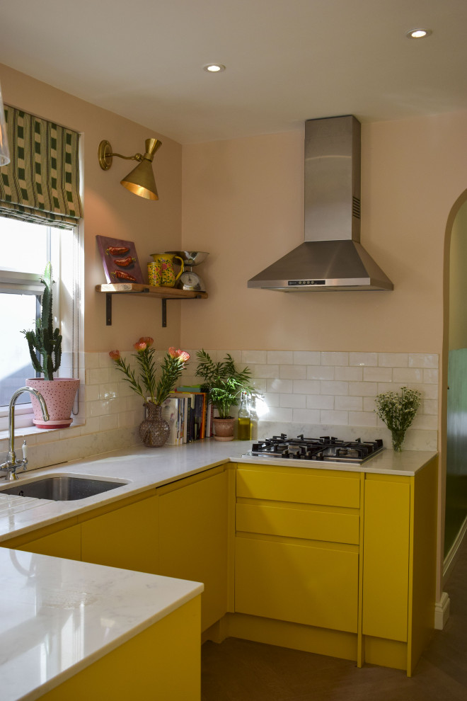 Design ideas for a mid-sized eclectic u-shaped open plan kitchen in London with flat-panel cabinets, yellow cabinets, marble benchtops, white splashback, ceramic splashback and white benchtop.