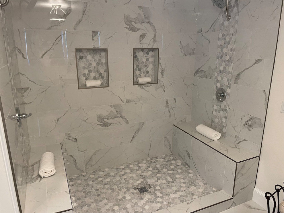 Walk-in marble shower with glass door, built-in benches, wall niches, hex tile floor, and mosaic accent strip.