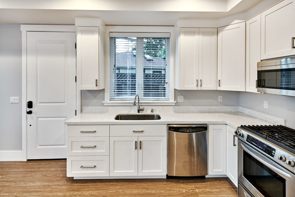 Small transitional l-shaped open plan kitchen in San Francisco with an undermount sink, shaker cabinets, white cabinets, quartz benchtops, stainless steel appliances, light hardwood floors, no island, brown floor and white benchtop.