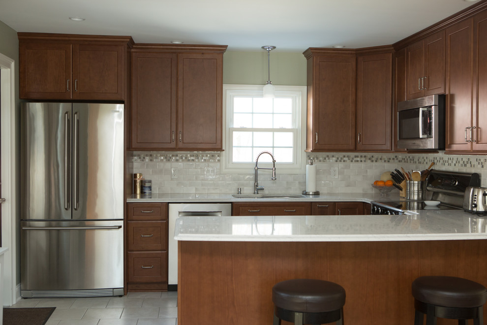 Example of a mid-sized transitional l-shaped white floor and ceramic tile eat-in kitchen design with an undermount sink, quartz countertops, white backsplash, stainless steel appliances, white countertops, shaker cabinets, medium tone wood cabinets, porcelain backsplash and a peninsula