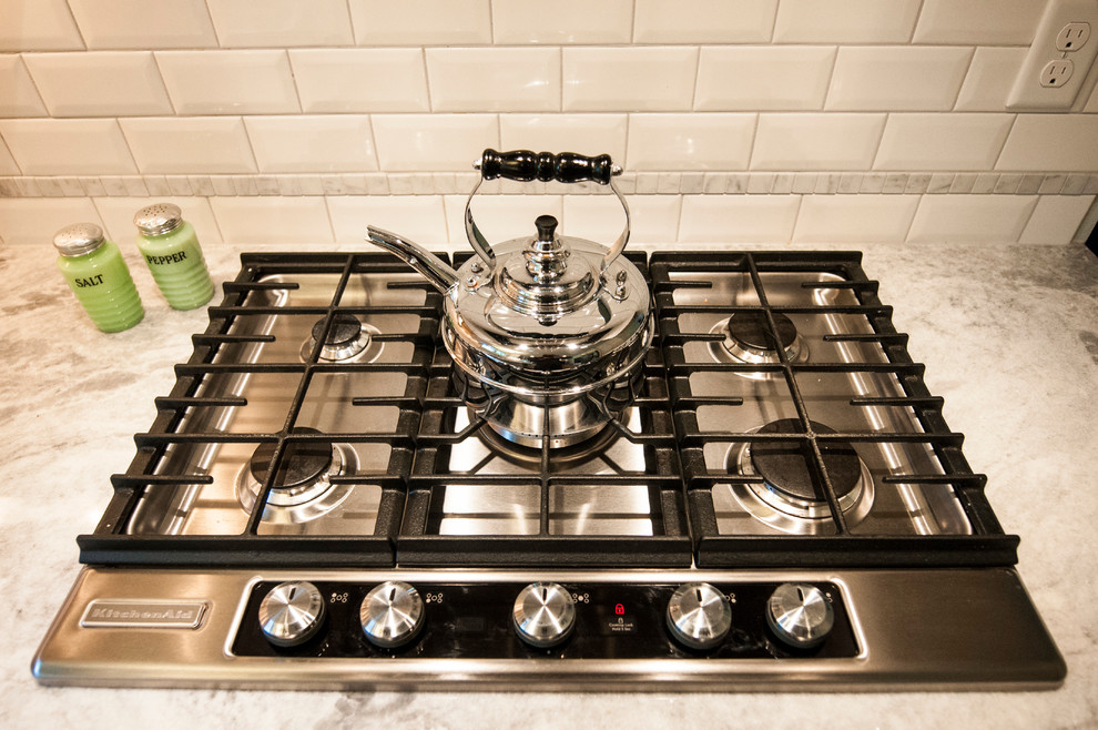 Inspiration for a small transitional u-shaped medium tone wood floor enclosed kitchen remodel in Milwaukee with a farmhouse sink, shaker cabinets, white cabinets, granite countertops, white backsplash, subway tile backsplash, stainless steel appliances and a peninsula